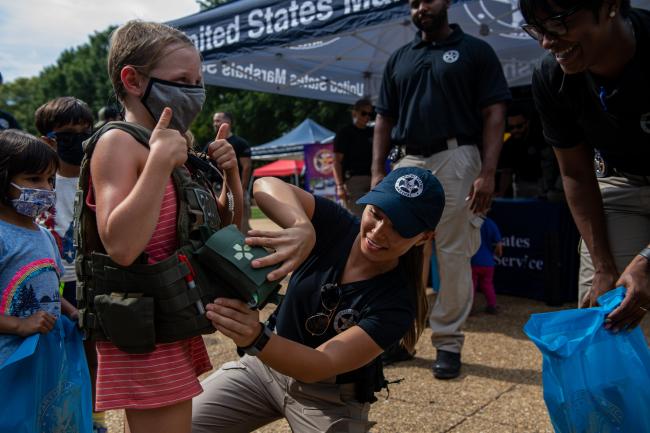 Deputy U.S. Marshal puts tactical vest on child during…
